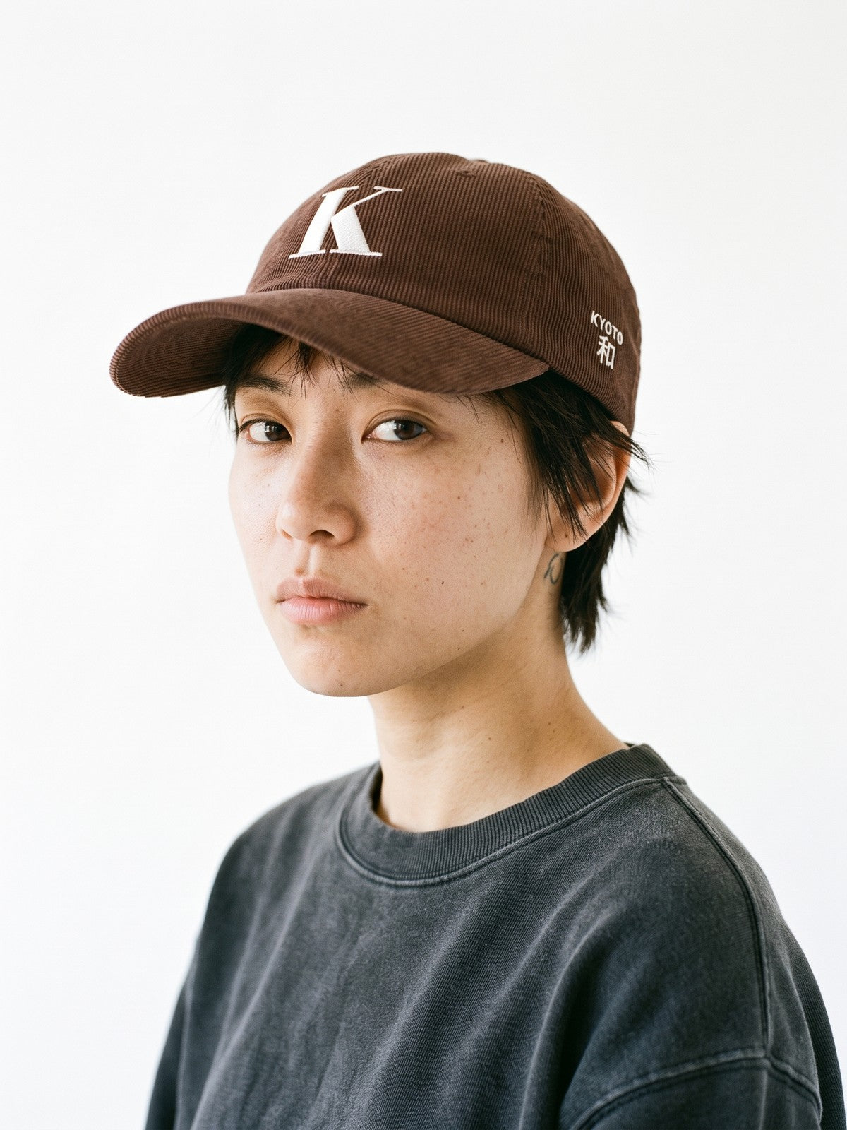 Model wearing the 5C5V Kyoto K Corduroy Japanese baseball cap in brown, a serif K embroidered on the front, KYOTO and 和 (harmony) on the left side
