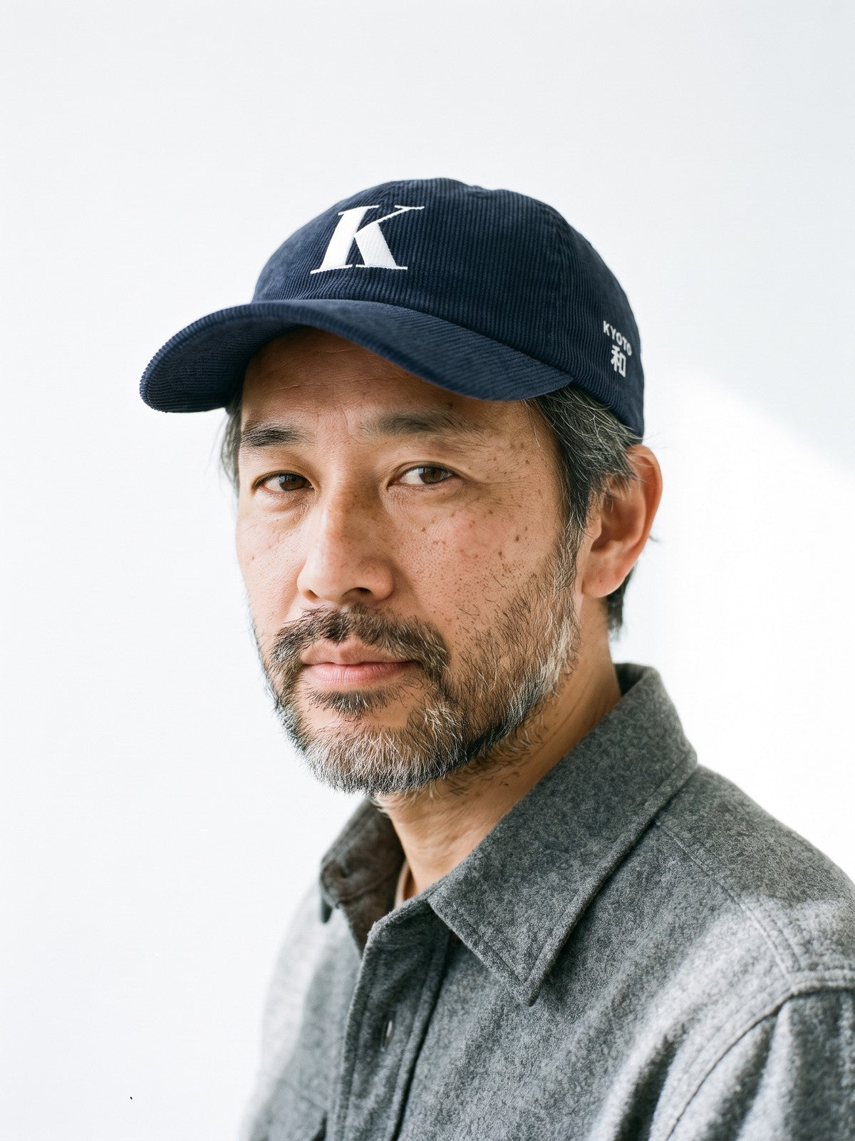 Model wearing the 5C5V Kyoto K Corduroy Japanese baseball cap in navy, a serif K embroidered on the front, KYOTO and 和 (harmony) on the left side