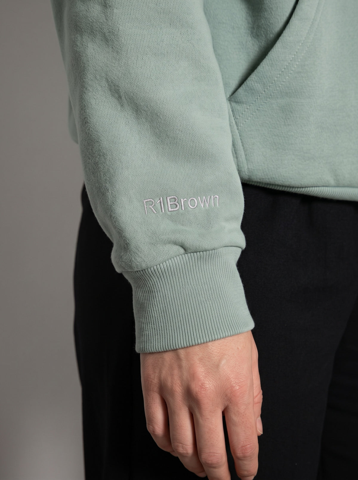 Close-up of the small R1Brown embroidery in grey thread on the right cuff of the 5C5V Originals Arona hoodie