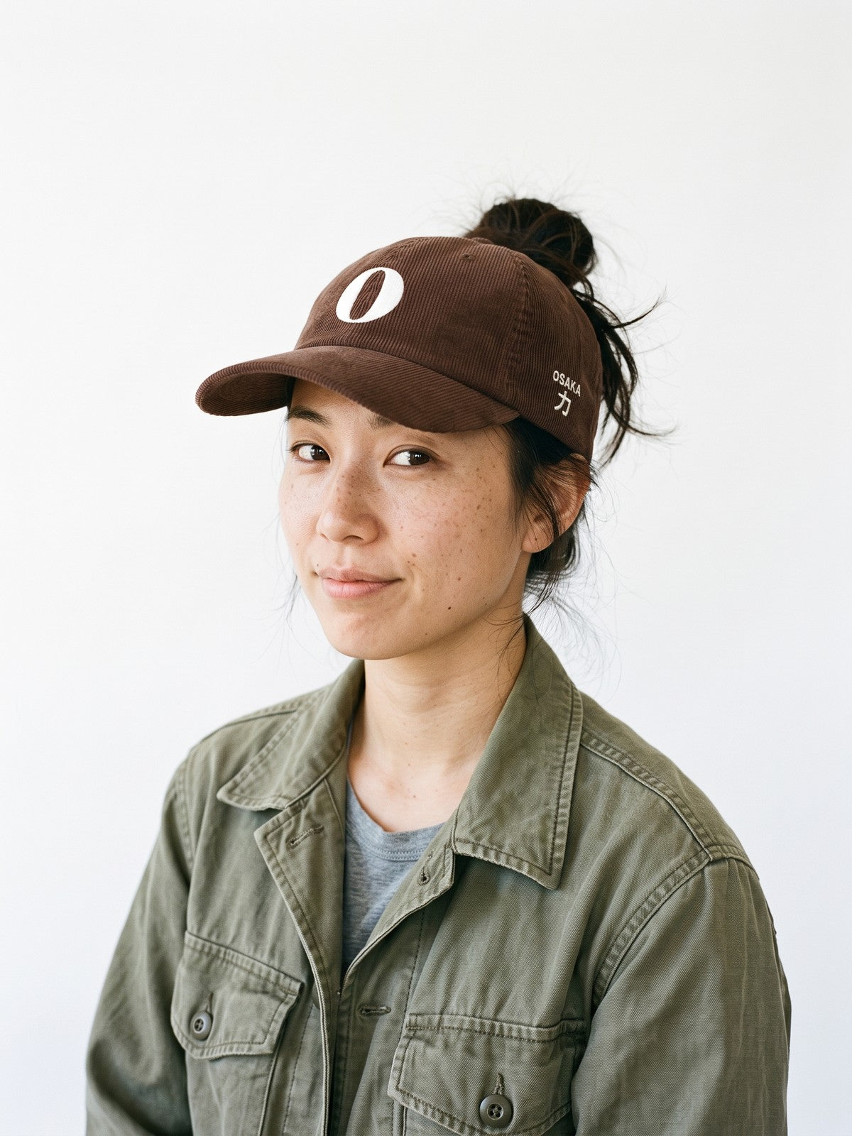 Model wearing the 5C5V Osaka O Corduroy Japanese baseball cap in brown, a serif O embroidered on the front, OSAKA and 力 (strength) on the left side