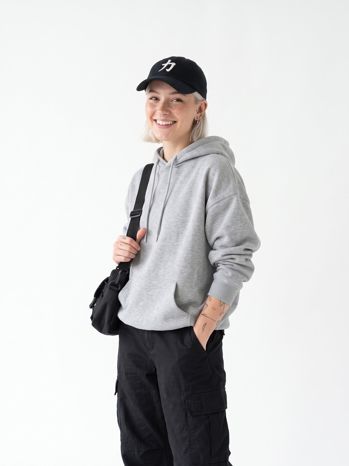 Model with a platinum bob in a grey hoodie and black cargos wearing the black 5C5V Osaka Strength 力 cap, three-quarter view