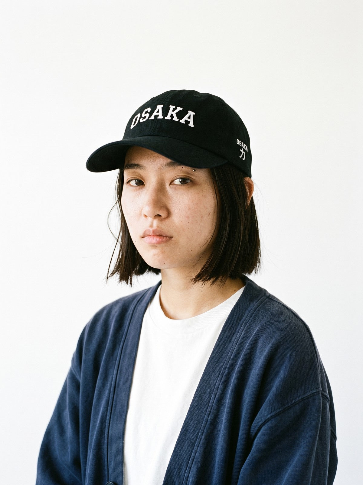 Model wearing the 5C5V Osaka Varsity Japanese baseball cap in black, OSAKA in arched varsity letters embroidered on the front, OSAKA and 力 (strength) on the left side