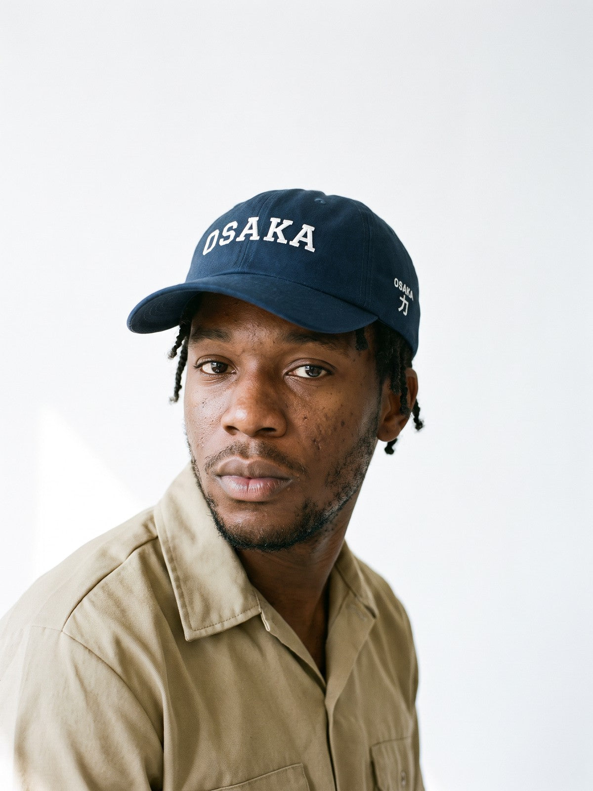 Model wearing the 5C5V Osaka Varsity Japanese baseball cap in navy, OSAKA in arched varsity letters embroidered on the front, OSAKA and 力 (strength) on the left side
