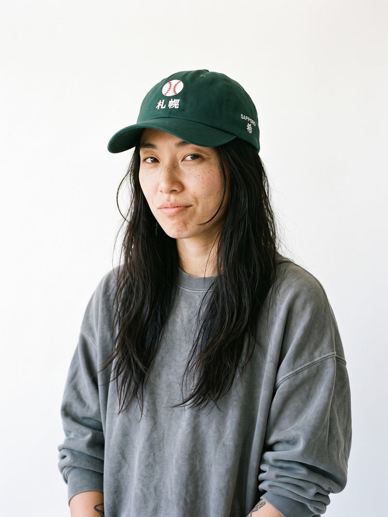 Model wearing the 5C5V Sapporo Ball Japanese baseball cap in spruce, a stitched baseball over 札幌 embroidered on the front, SAPPORO and 希 (hope) on the left side