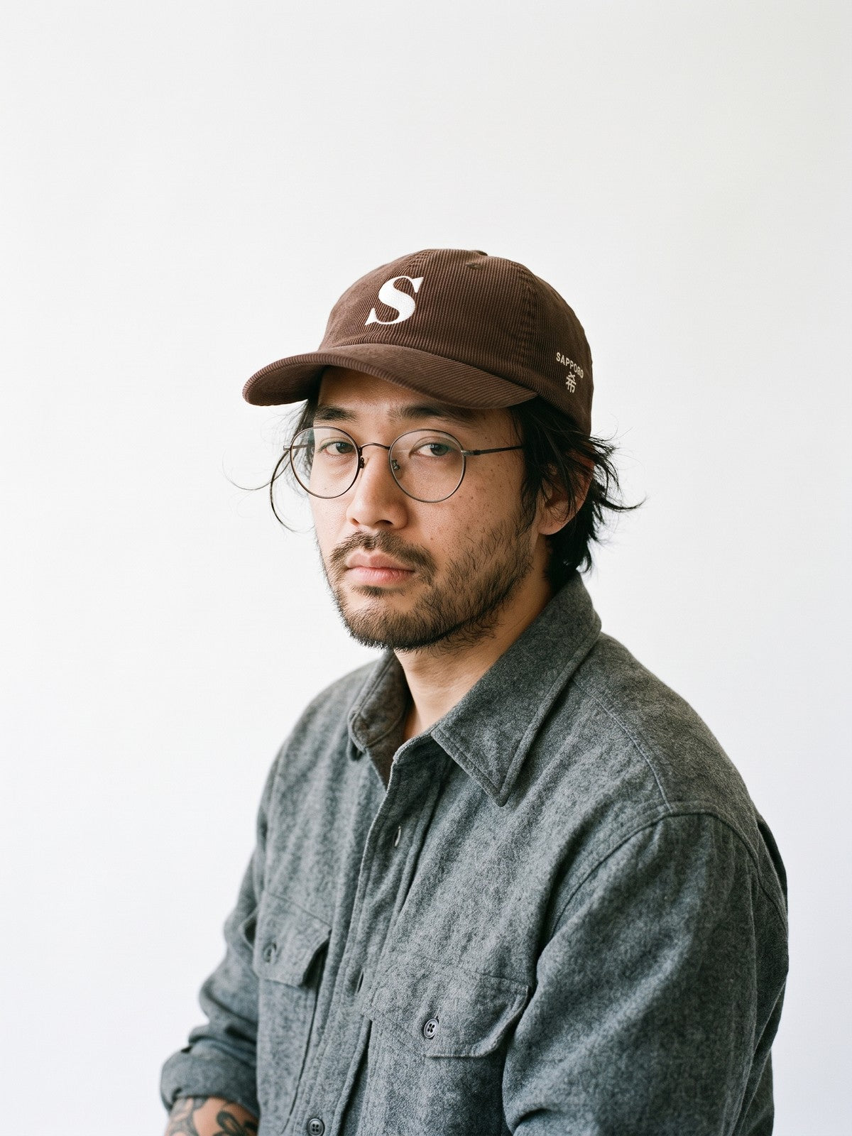 Model wearing the 5C5V Sapporo S Corduroy Japanese baseball cap in brown, a serif S embroidered on the front, SAPPORO and 希 (hope) on the left side