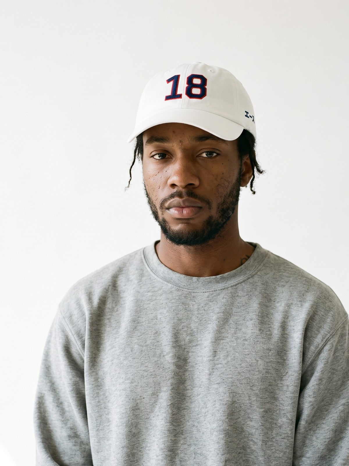 Model wearing the 5C5V Ace 18 Japanese baseball cap in white, 18 embroidered in navy with a red outline on the front, エース (ace) in navy on the left side