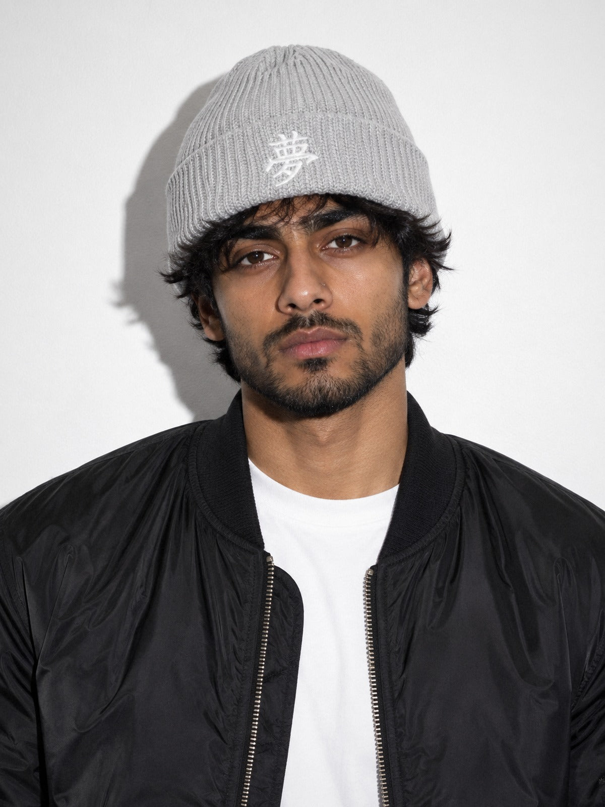 Model in a black bomber jacket wearing the Grey 5C5V Tokyo Dream beanie with 夢 embroidered in white on the cuff, front view