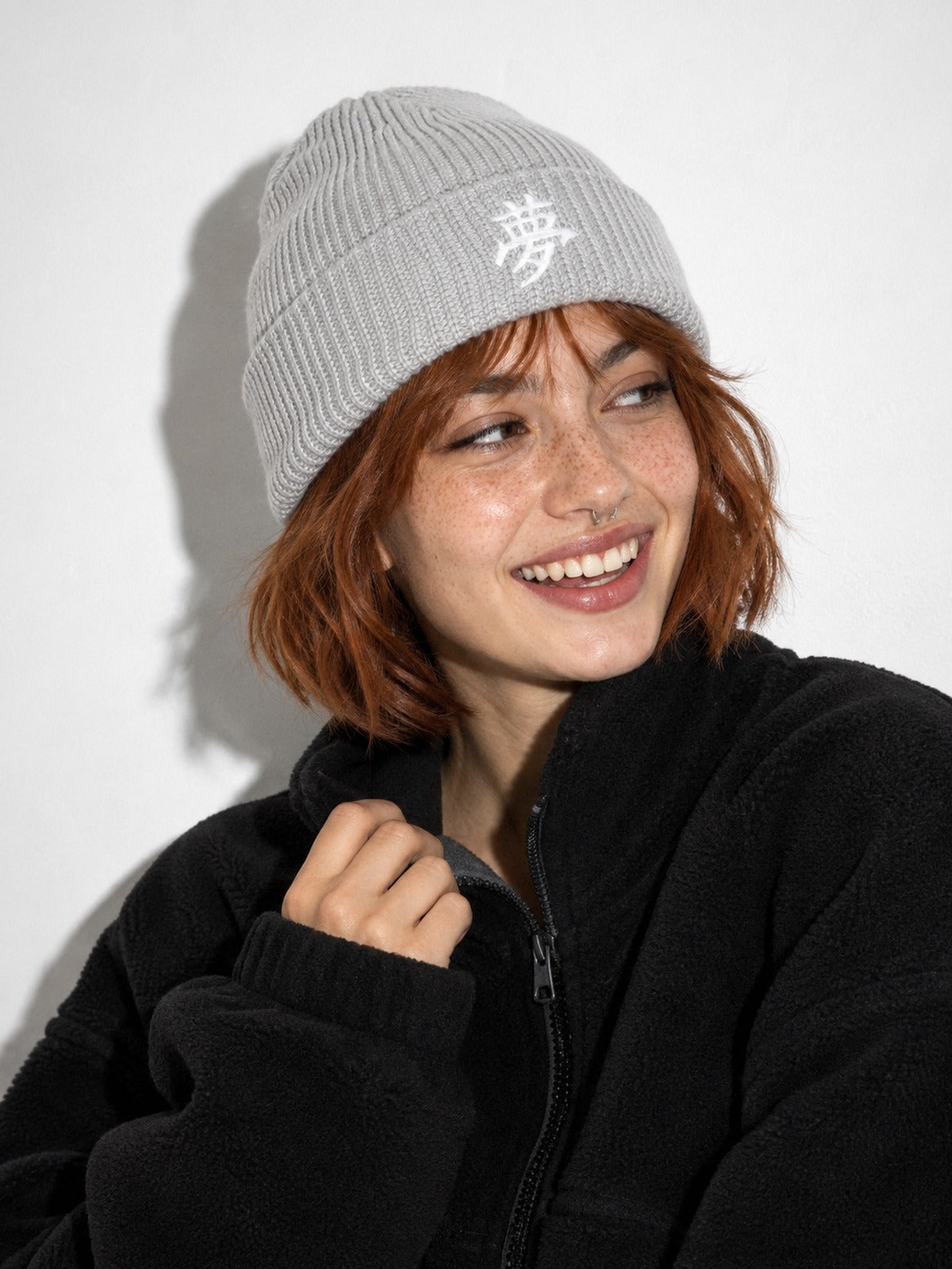 Laughing model with a copper bob in a black fleece wearing the Grey 5C5V Tokyo Dream 夢 beanie, three-quarter view