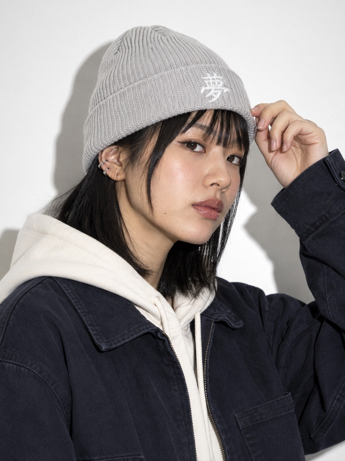 Model in a navy chore jacket touching the cuff of the Grey 5C5V Tokyo Dream 夢 beanie, side angle