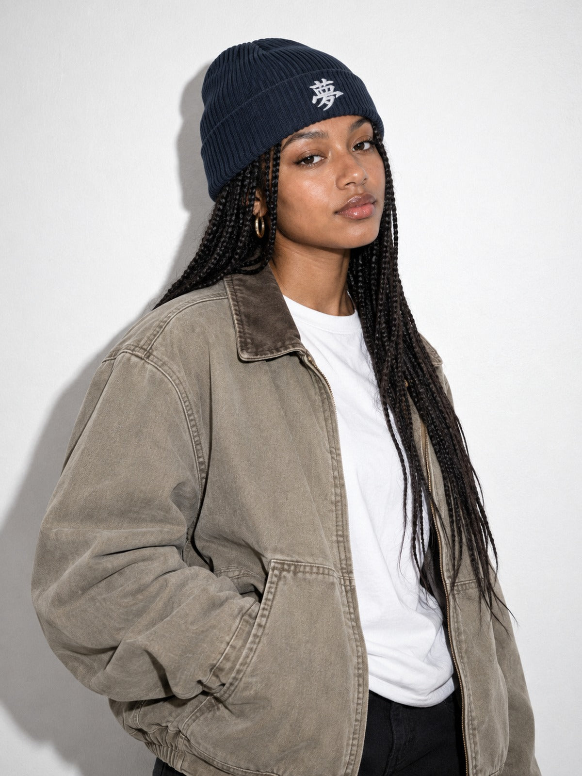 Model with long box braids in a canvas work jacket wearing the Navy 5C5V Tokyo Dream 夢 beanie, three-quarter view