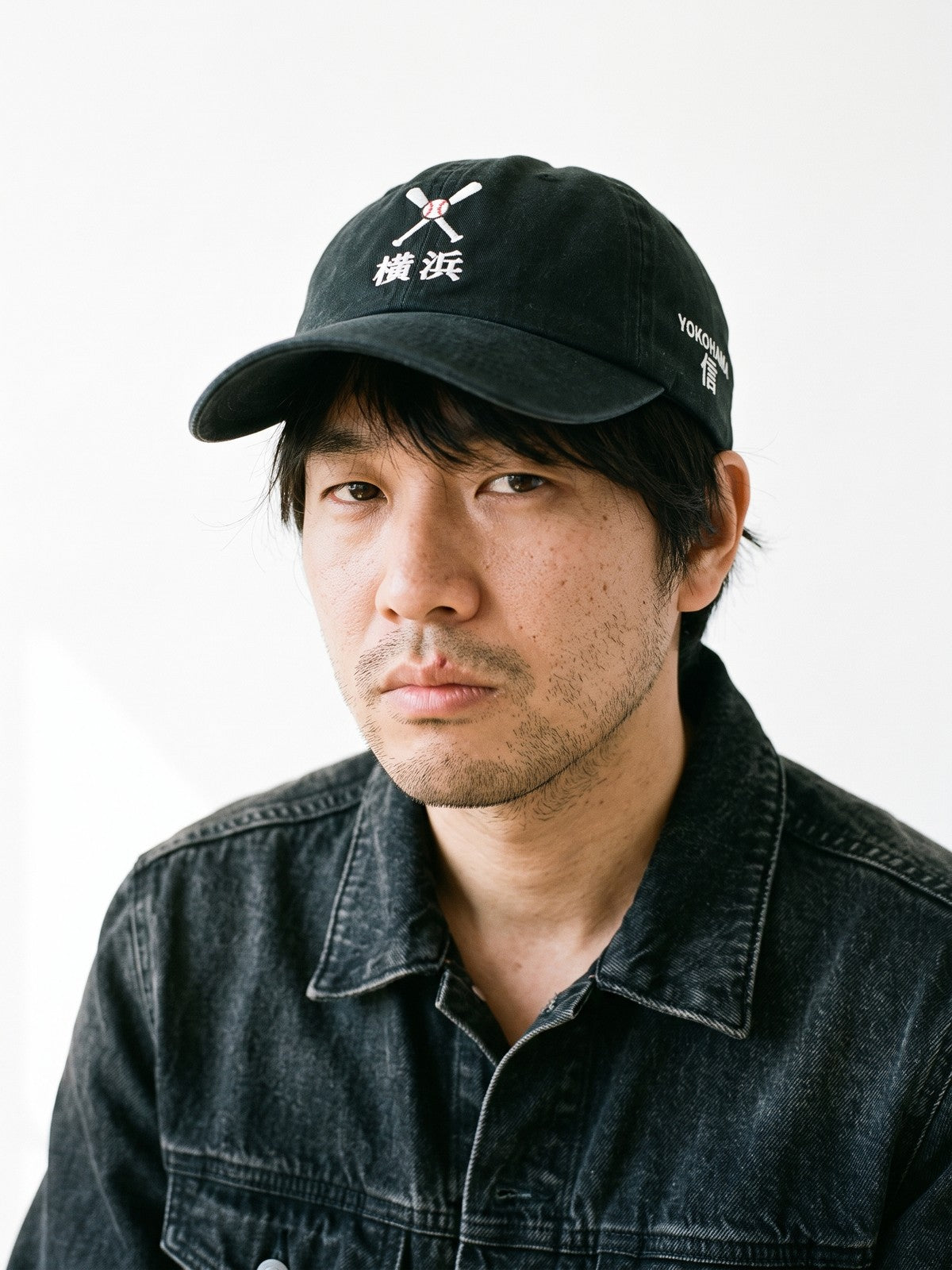 Model wearing the 5C5V Yokohama Crossed Bats Japanese baseball cap in black, crossed bats over 横浜 embroidered on the front, YOKOHAMA and 信 (trust) on the left side