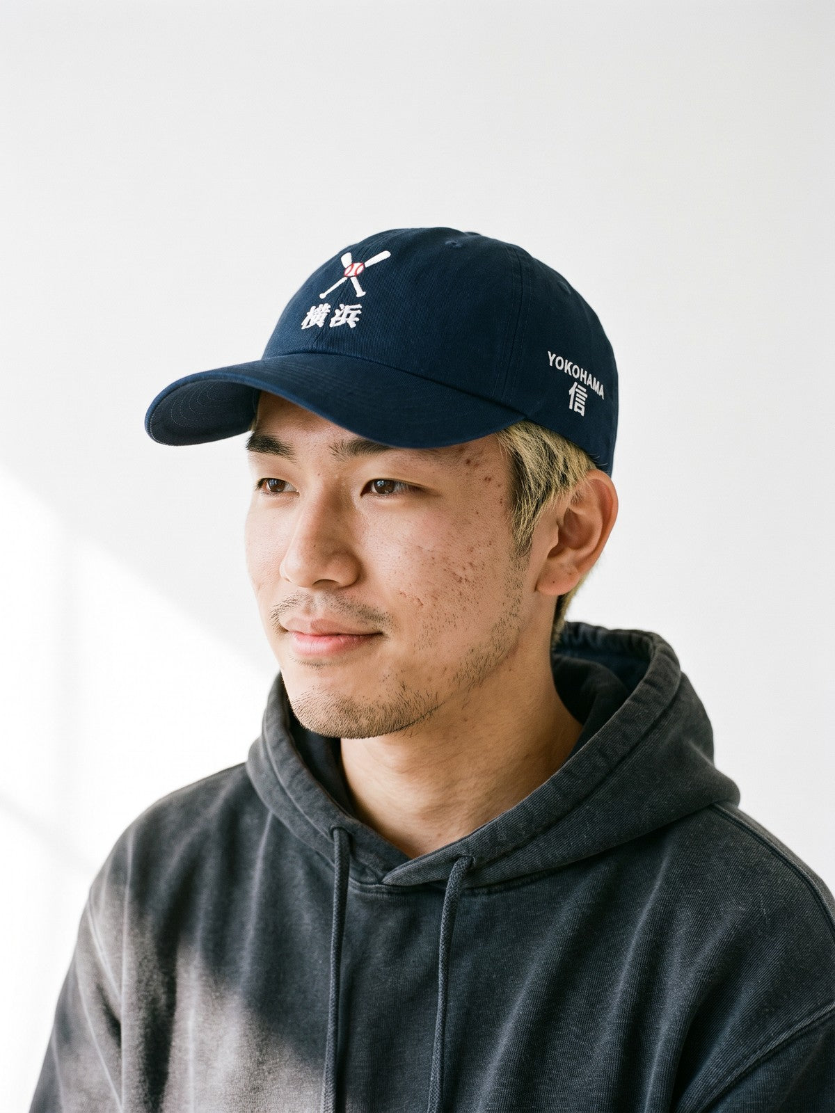Model wearing the 5C5V Yokohama Crossed Bats Japanese baseball cap in navy, crossed bats over 横浜 embroidered on the front, YOKOHAMA and 信 (trust) on the left side