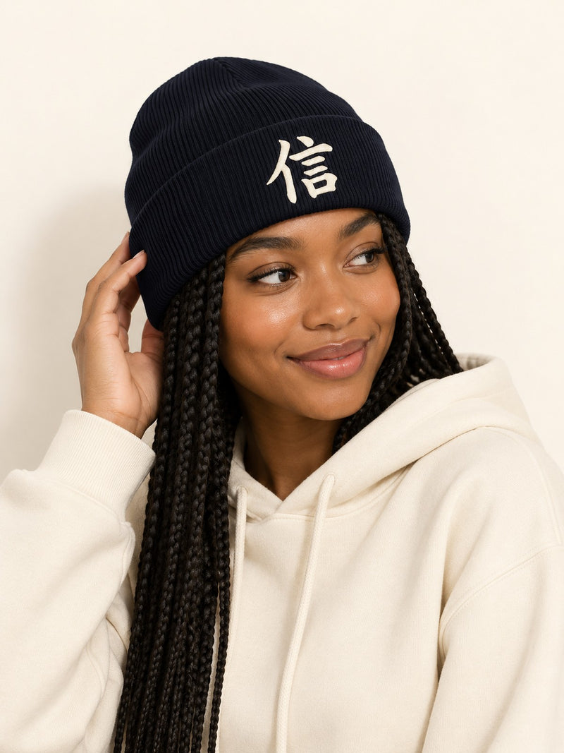 Smiling model with long box braids in a cream hoodie wearing the navy 5C5V Yokohama Trust beanie with 信 embroidered in cream on the cuff, three-quarter view
