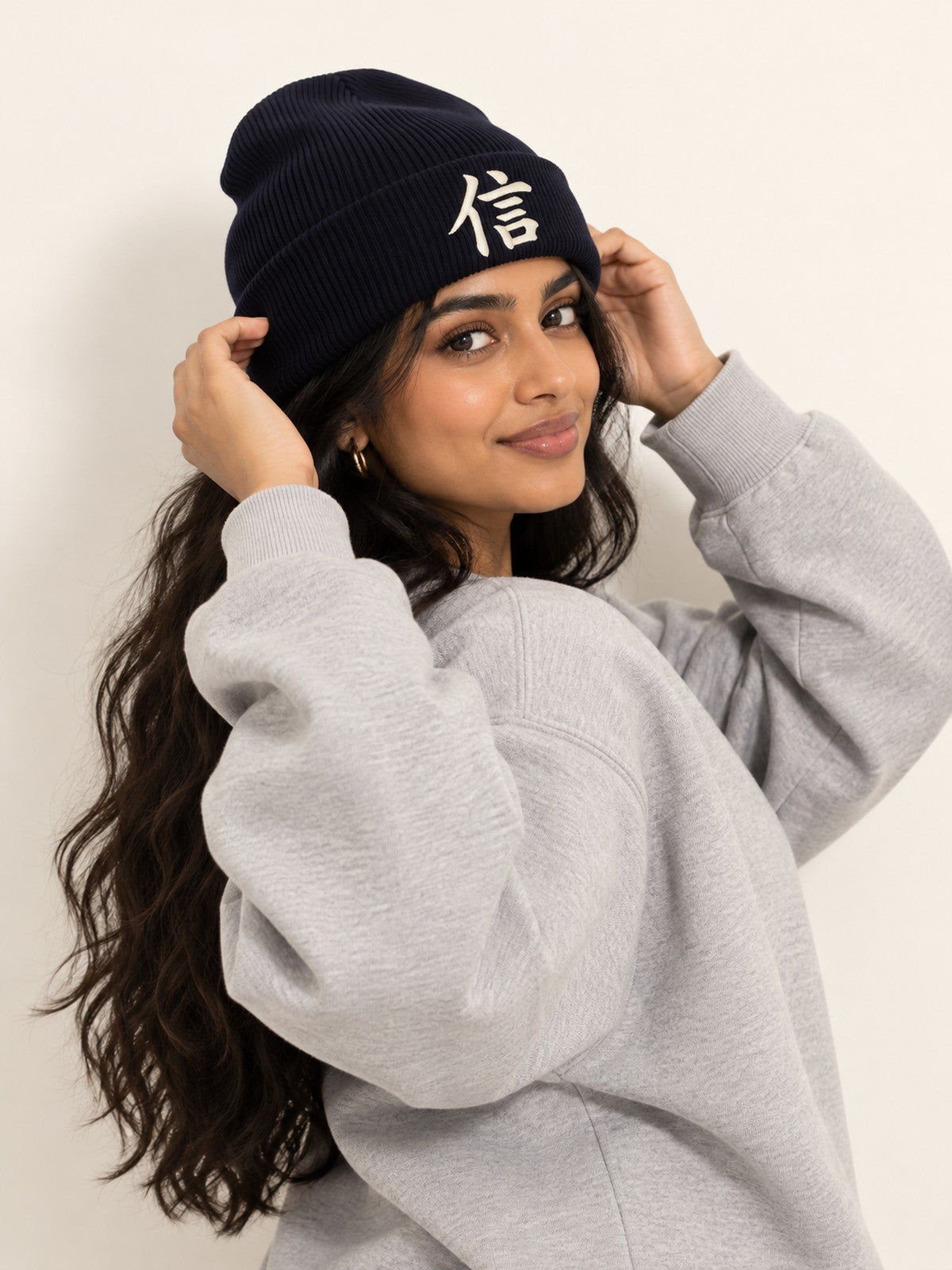 Model with long wavy hair in a grey sweatshirt adjusting the navy 5C5V Yokohama Trust 信 beanie, side angle