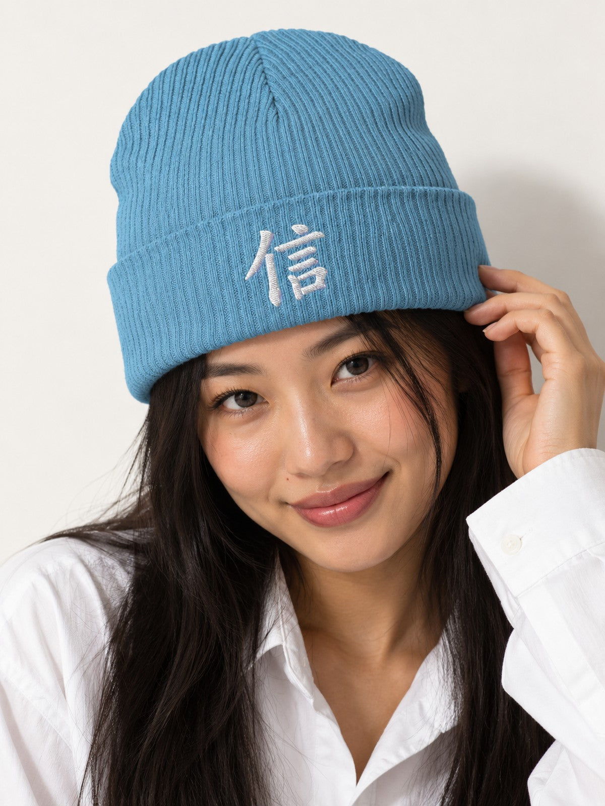 Close-up of the white embroidered kanji 信 (trust) on the Light Avio Blue 5C5V Yokohama ribbed beanie, model in a white shirt touching the cuff