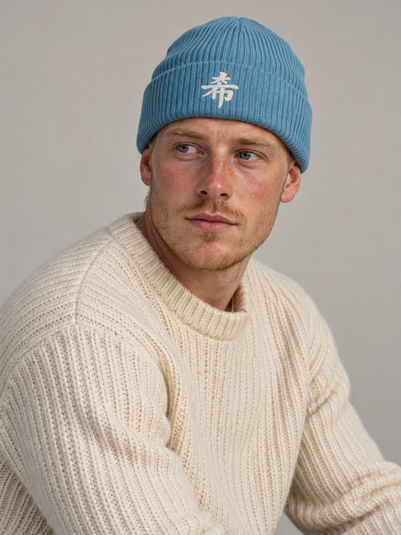 Model wearing the Light Avio Blue Sapporo Hope 希 ribbed beanie in the studio, white 3D-puff 希 embroidered on the cuff
