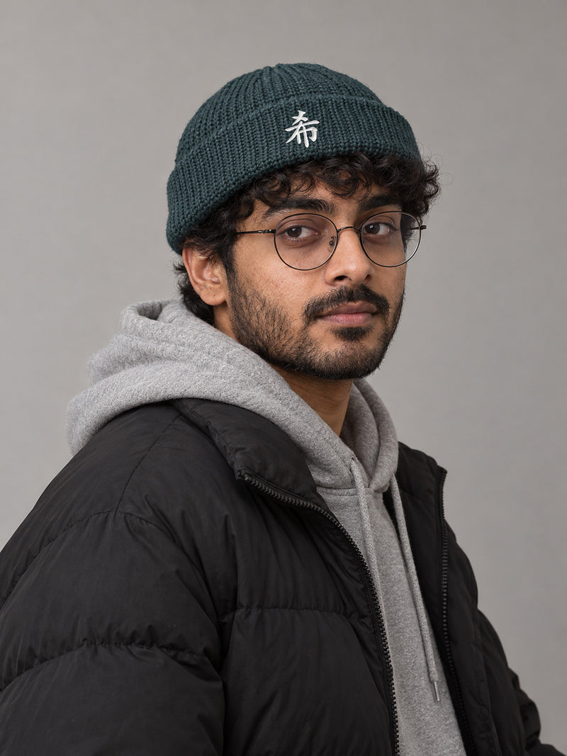 Model wearing the Petrol Blue Sapporo Hope 希 fisherman beanie in the studio, white satin-stitch 希 embroidered on the cuff
