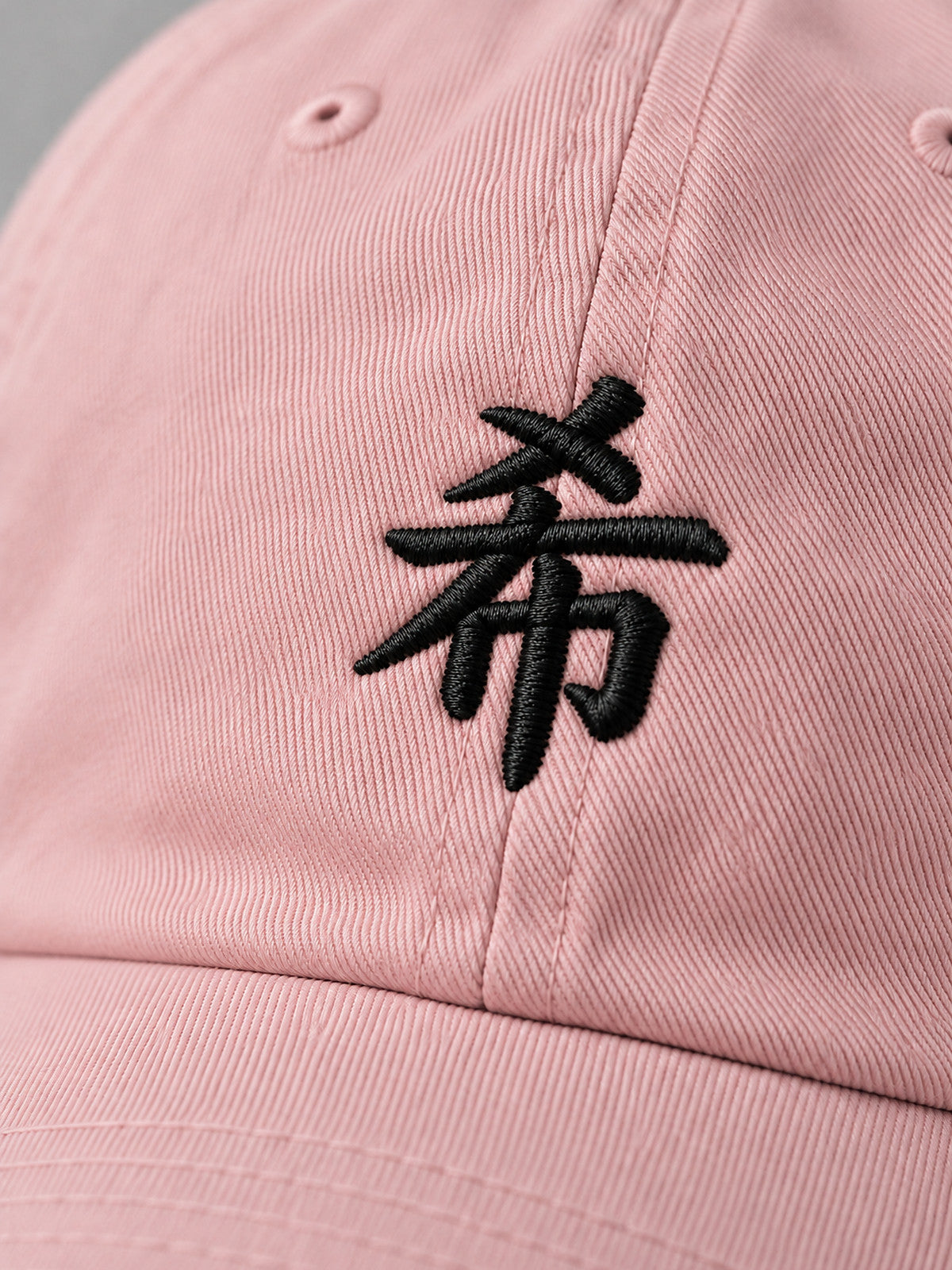 Close-up of the black 希 embroidery on the pastel pink First Light cap