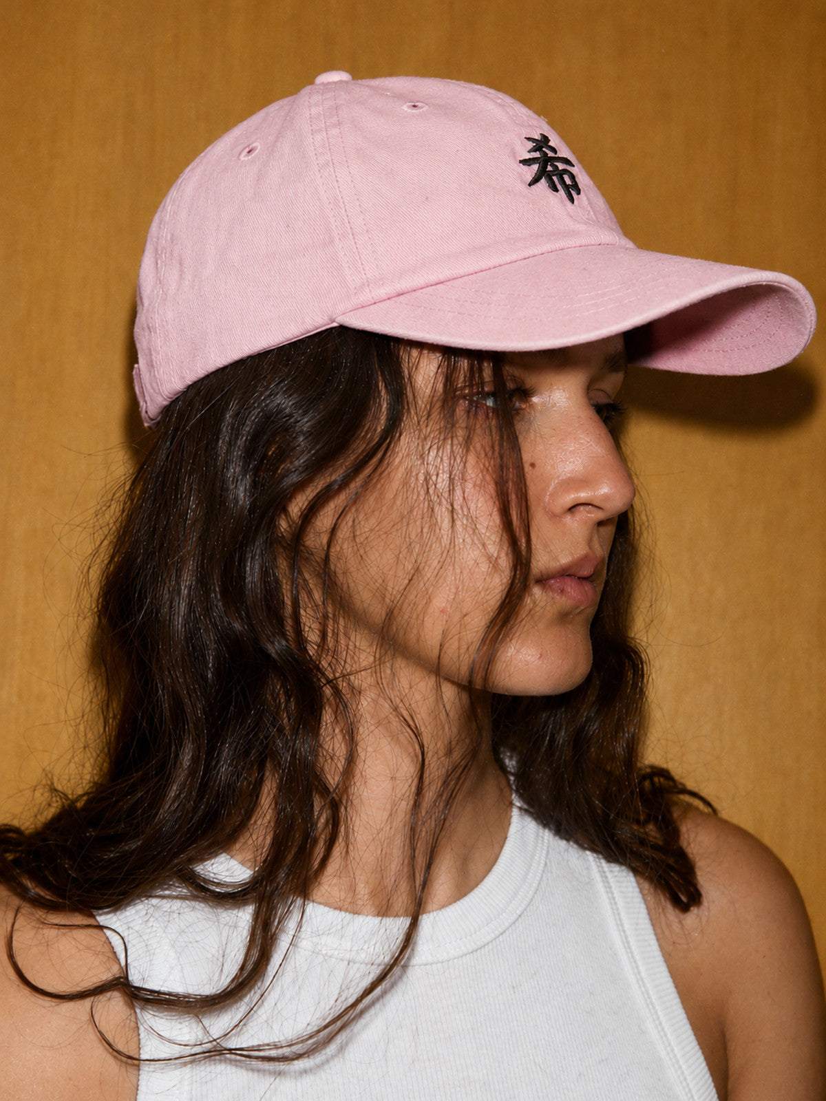 Model with long hair wearing the pastel pink First Light 希 cap, side view