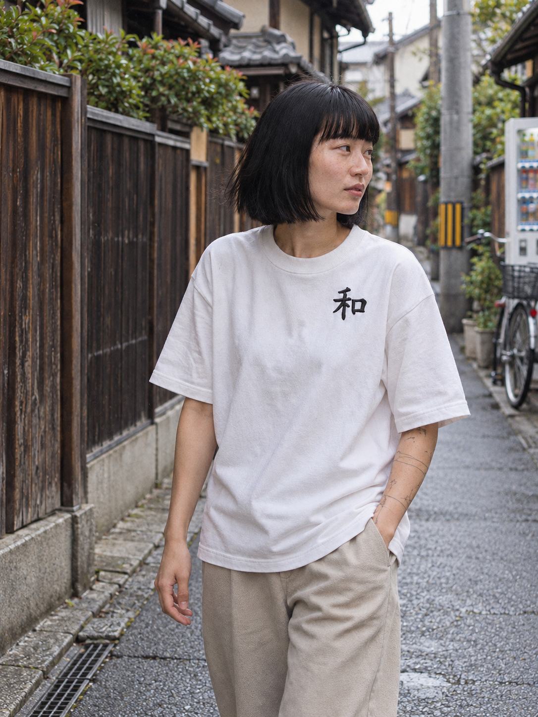 Model in the white Kyoto Harmony 和 tee walking down a quiet Kyoto backstreet lined with wooden fences