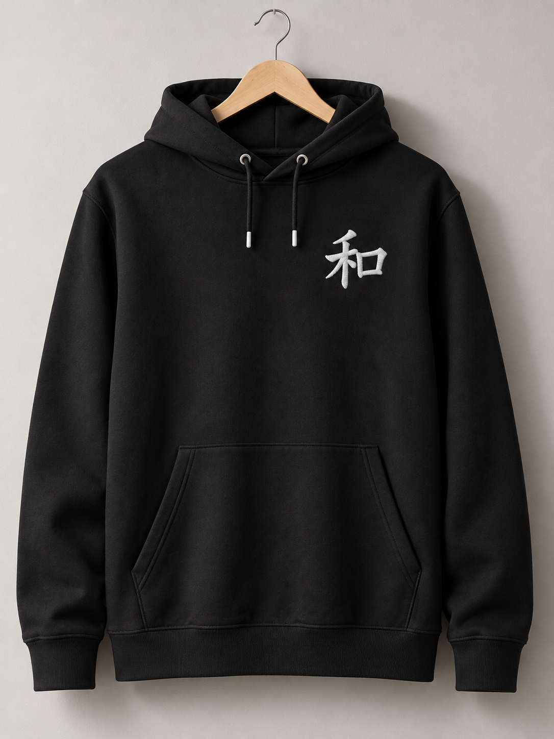 Black Kyoto Harmony 和 hoodie on a wooden hanger, front view with the small white embroidered 和 on the left chest