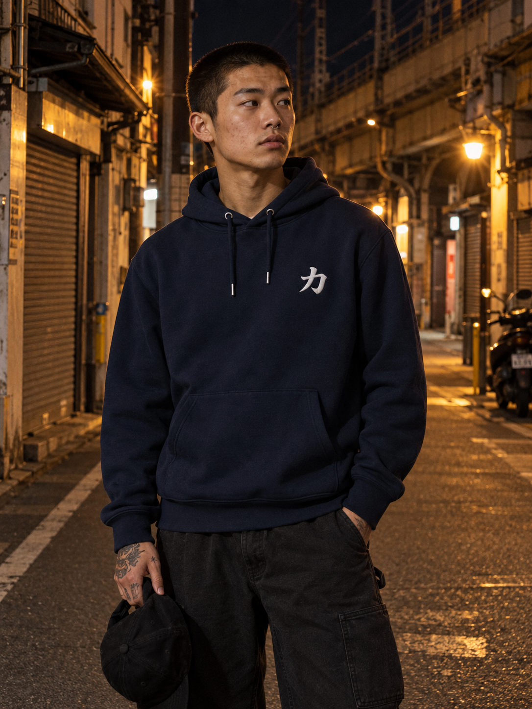 Model wearing the French Navy Osaka Strength 力 hoodie on a street under an Osaka railway viaduct at night