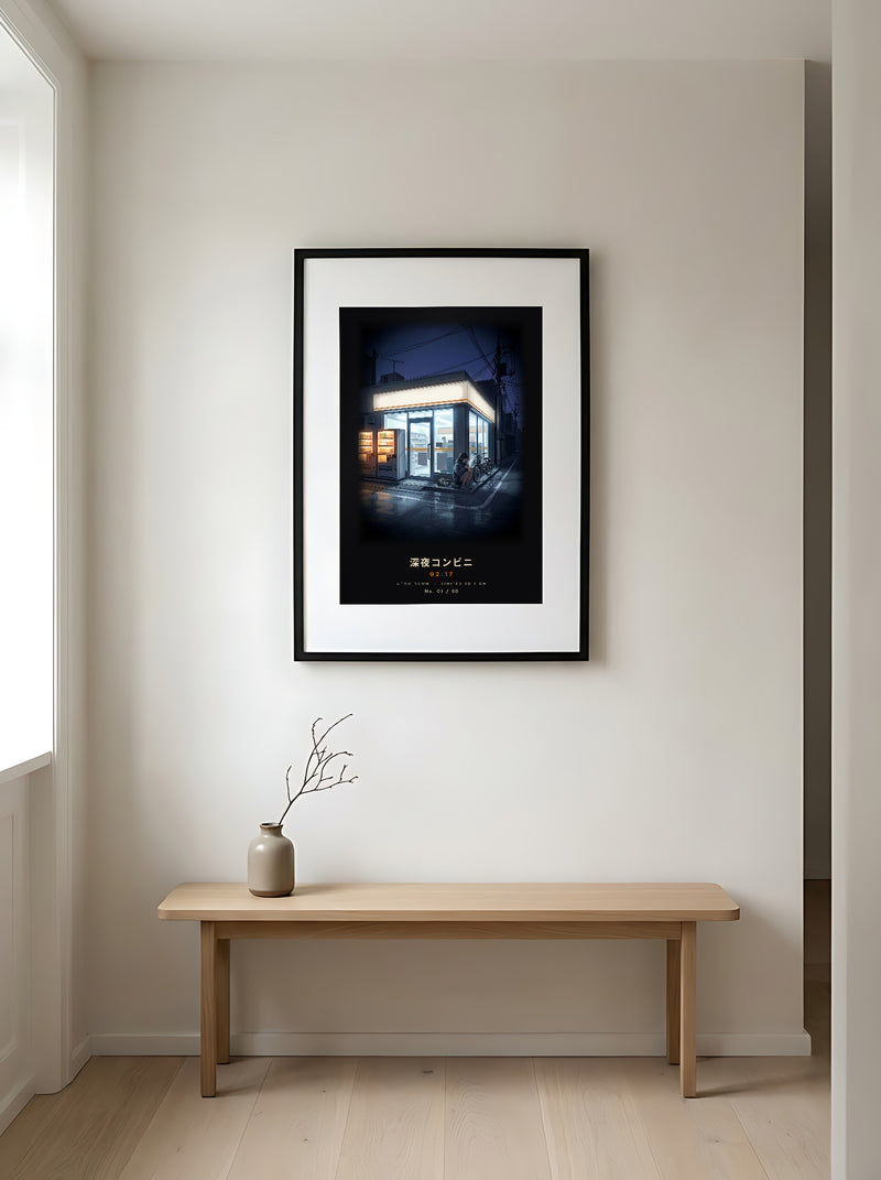 Shin'ya Konbini 深夜コンビニ limited edition framed print: a girl with a cup noodle outside a glowing Tokyo convenience store at 2am, black frame in a Japandi entryway above an oak bench