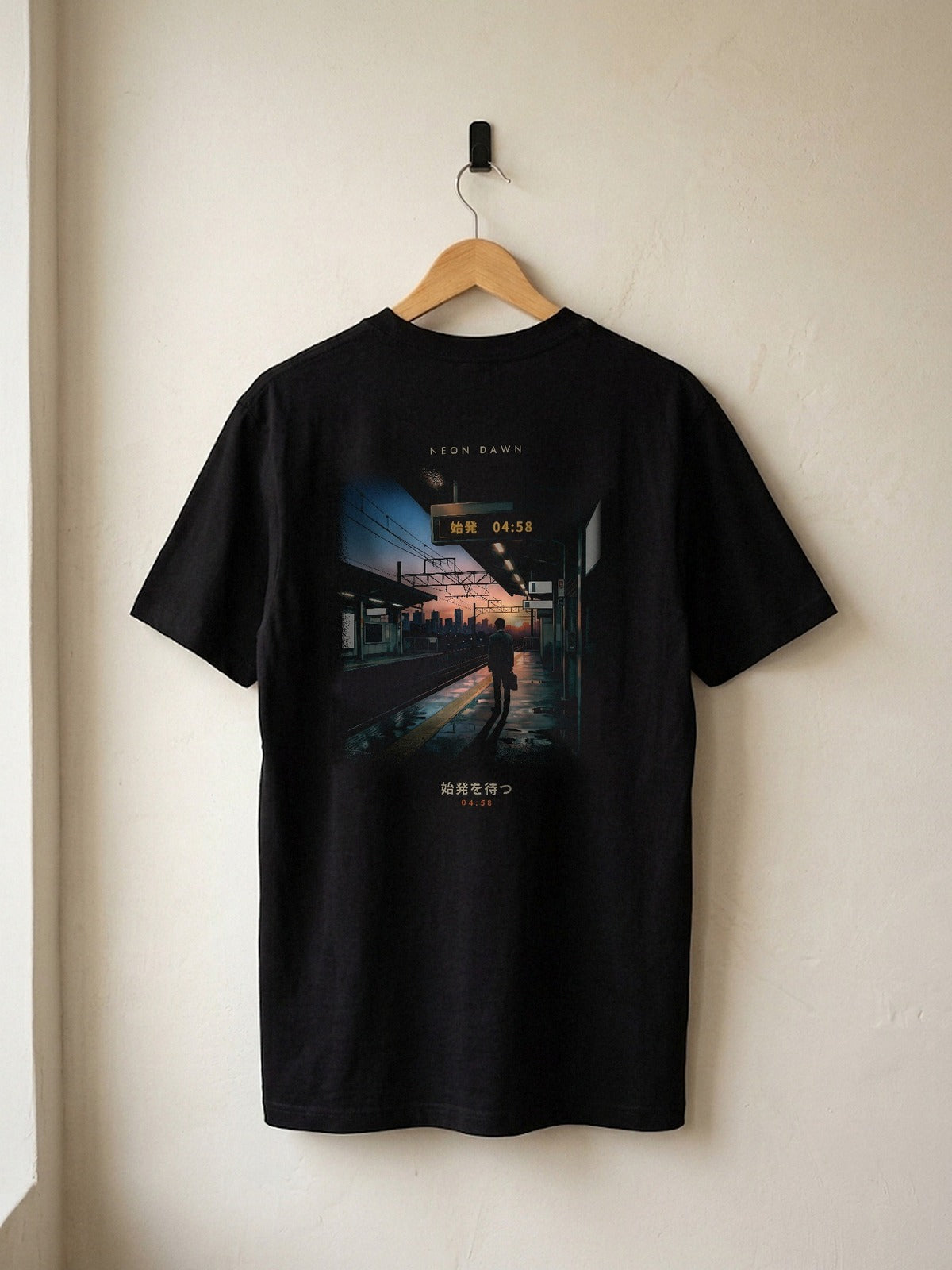 Neon Dawn Shihatsu 始発 heavyweight black tee on a wooden hanger against a plaster wall, showing the 04:58 Tokyo first-train back print
