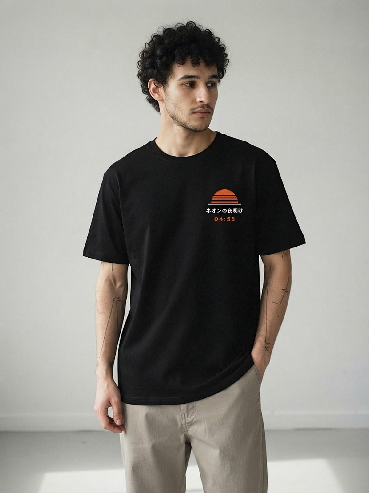 Model wearing the Neon Dawn Shihatsu 始発 black tee, front view with the embroidered 04:58 Neon Dawn sun on the chest