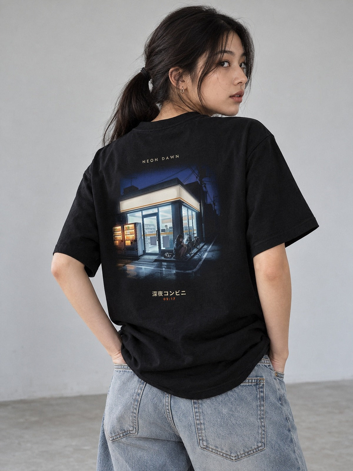 Model wearing the Neon Dawn Shin'ya Konbini black T-shirt from the back, showing the late-night Tokyo convenience store print with 深夜コンビニ and 02:17