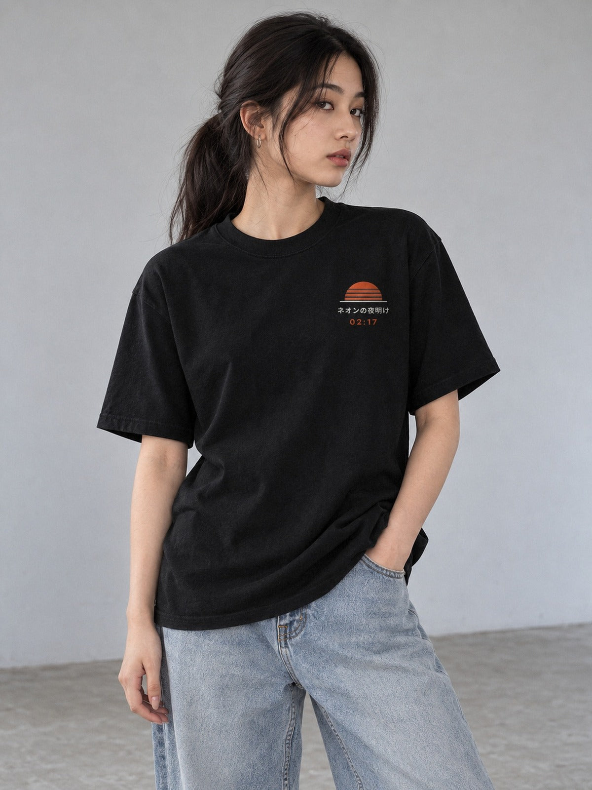 Model wearing the Neon Dawn Shin'ya Konbini black T-shirt from the front, with the small embroidered sunrise, ネオンの夜明け and orange 02:17 on the left chest