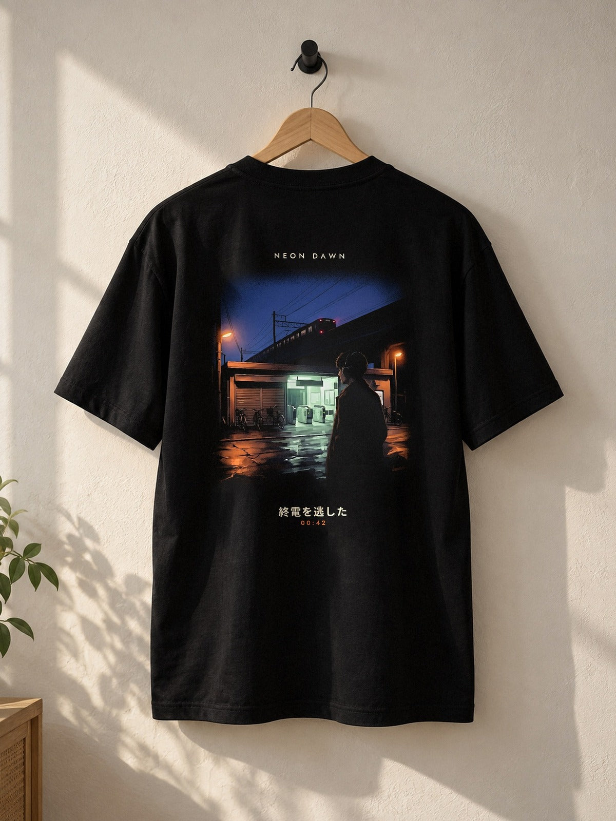 Back of the Shūden tee on a wooden hanger: a Tokyo station after the last train, NEON DAWN above and 終電を逃した 00:42 below