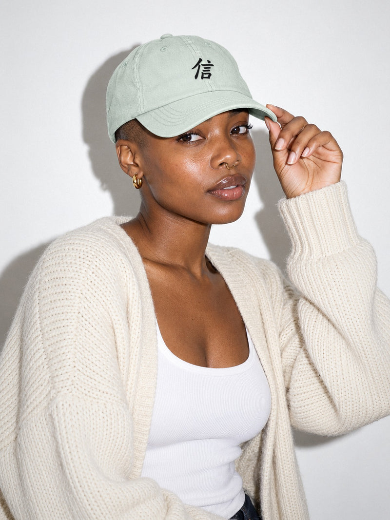 Model in a cream cardigan wearing the Pale North 信 pastel mint low pro cap, black 信 (trust) kanji embroidered on the front