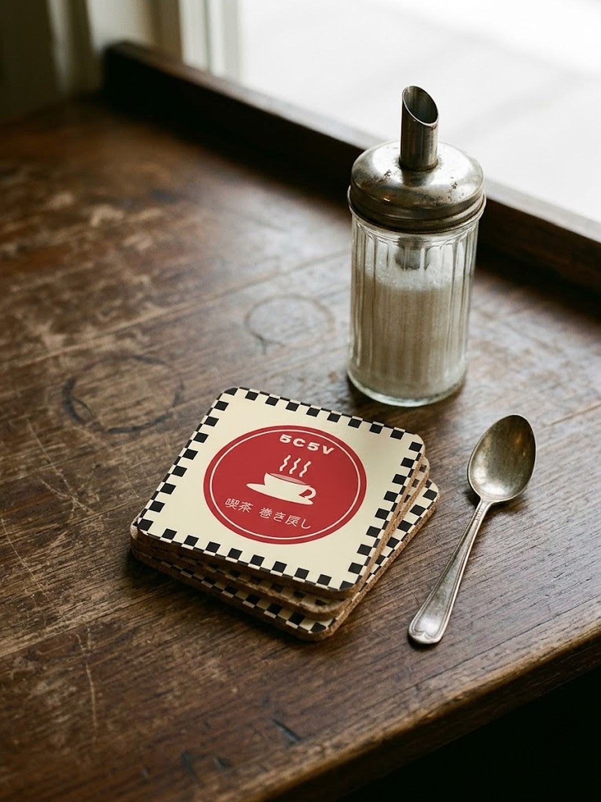 Stack of Kissaten 喫茶 Japanese Coffee Coasters by 5C5V on a worn café counter with a sugar shaker and teaspoon