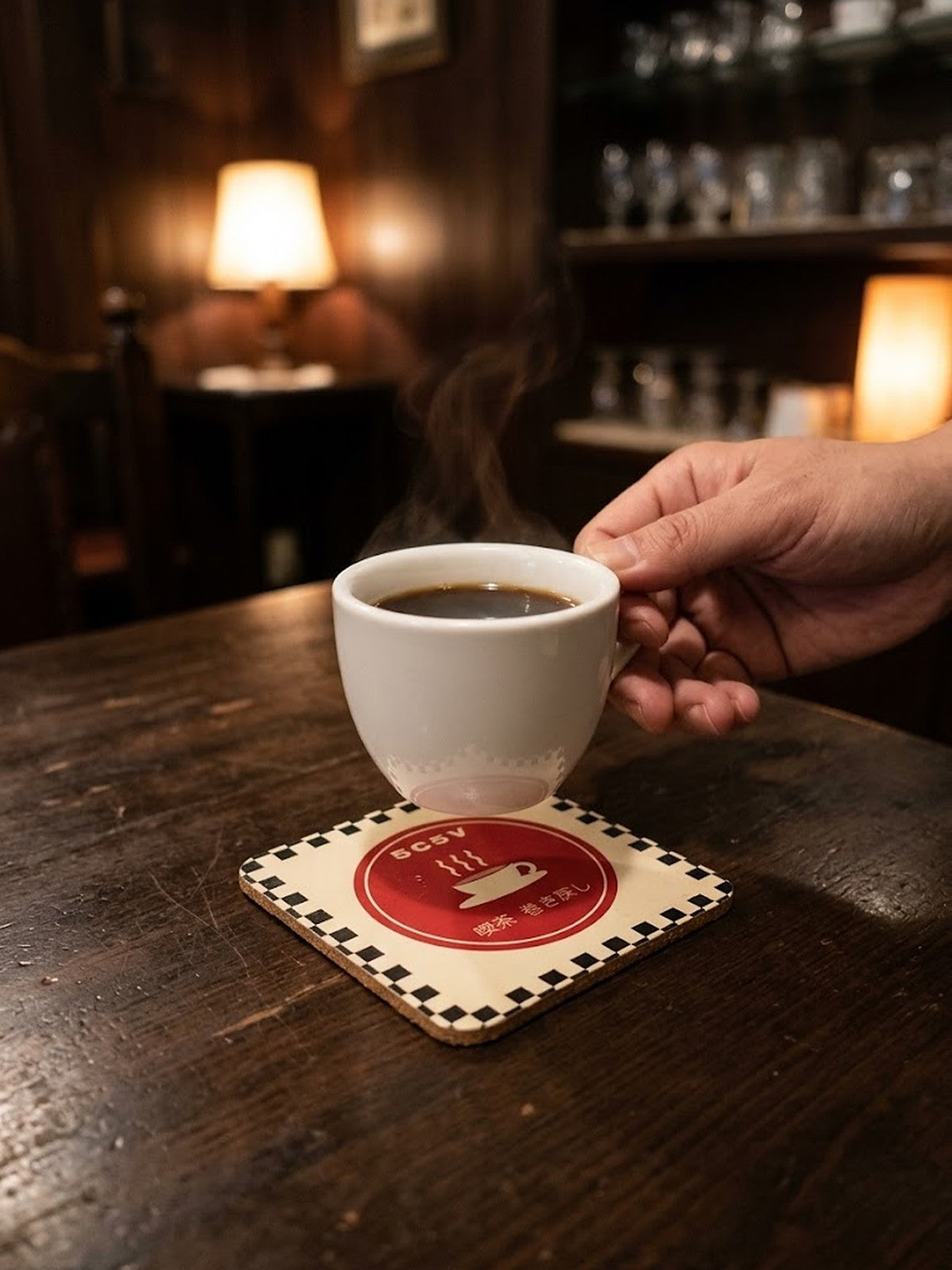 Hand setting a cup of black coffee on the Kissaten 喫茶 Japanese Coffee Coaster by 5C5V in a dim coffee shop