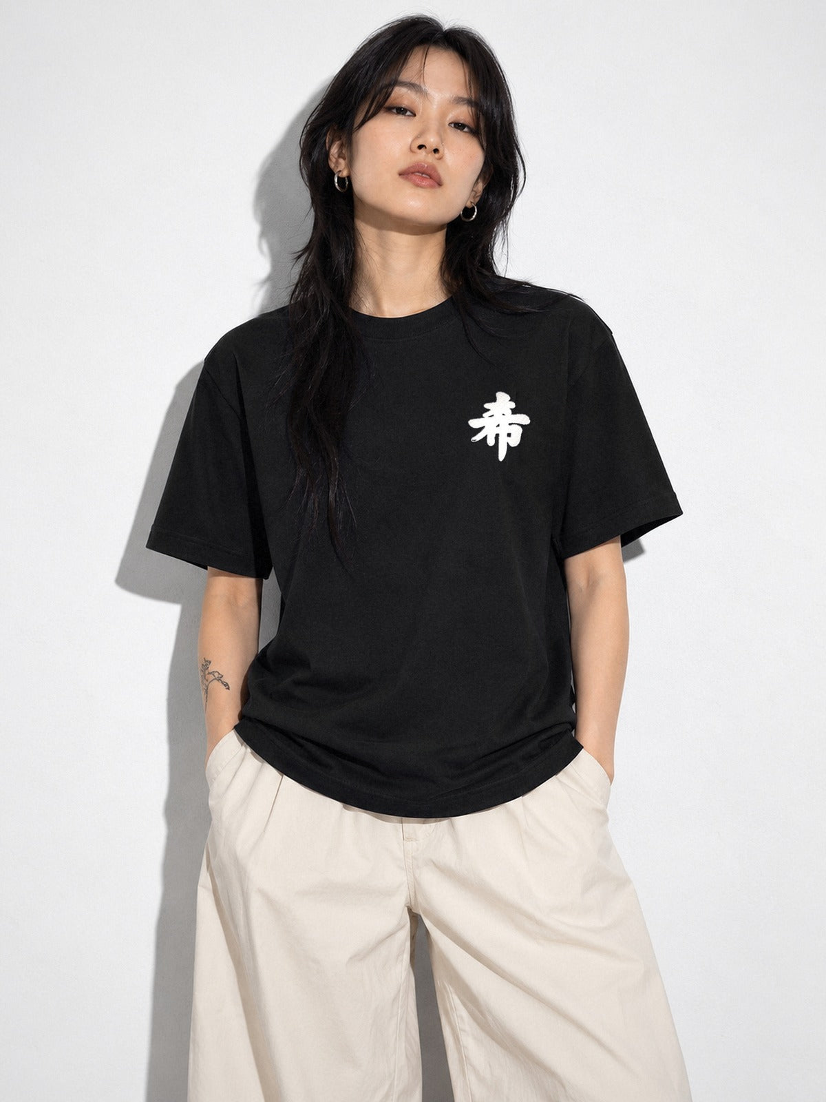 Model with a long black wolf cut wearing the black Sapporo Hope 希 premium oversized tee, white 希 kanji embroidered on the chest
