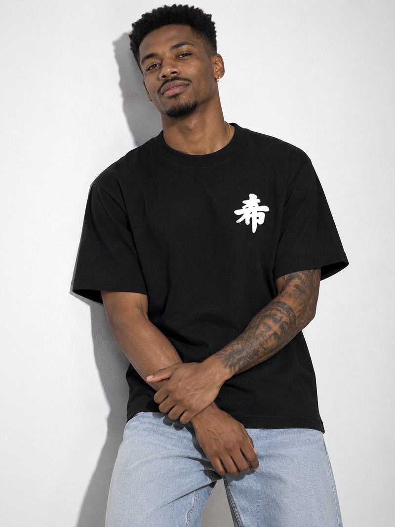 Model leaning on a white wall in the black Sapporo Hope 希 premium oversized tee