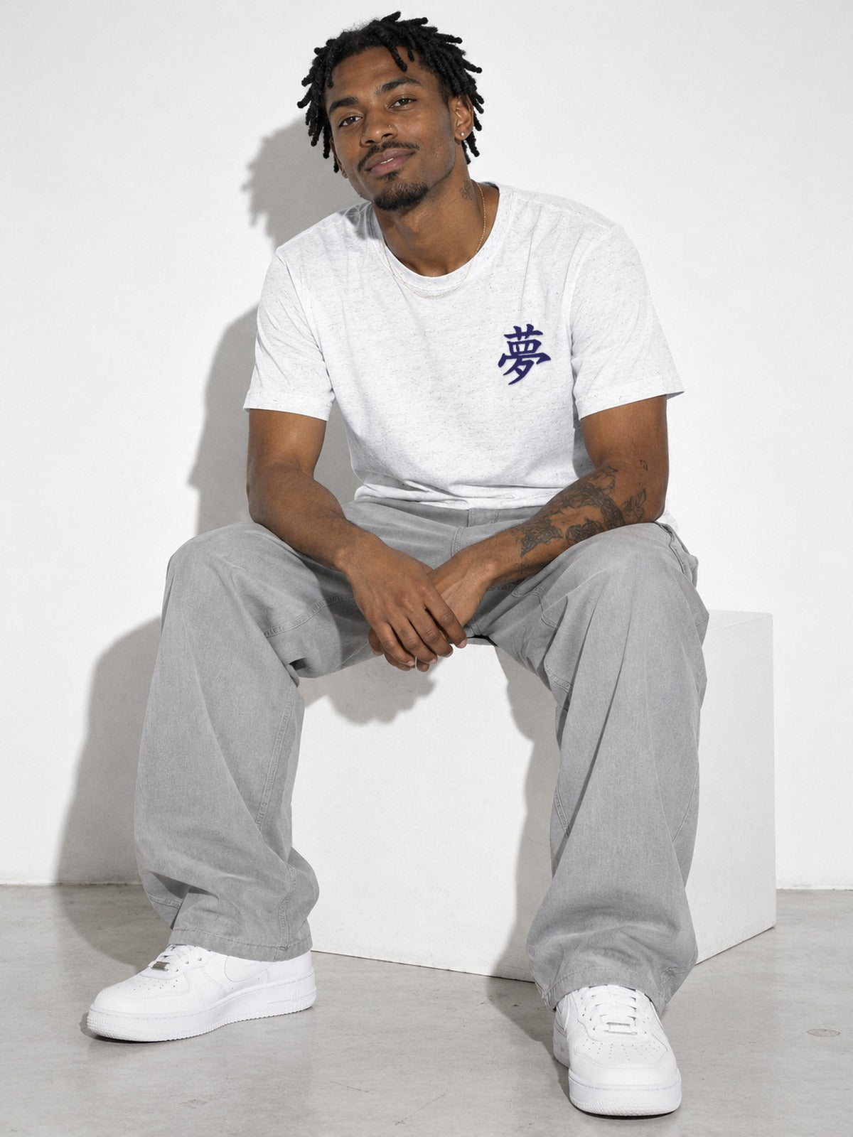 Model sitting on a white block in the white Tokyo Dream 夢 embroidered tee