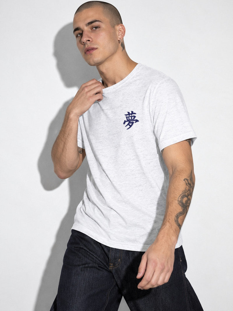 Model with a shaved head in the white Tokyo Dream 夢 tee, close view of the navy chest embroidery